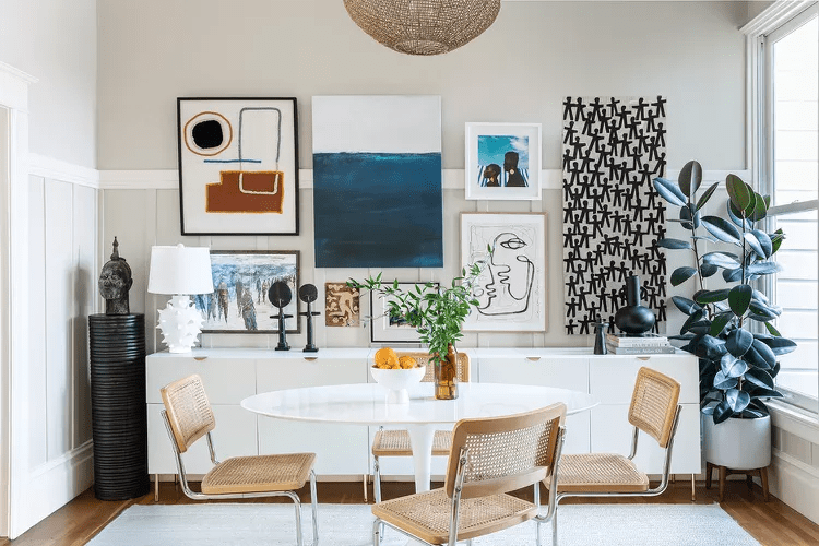 a horizontal line gallery wall idea in a modern dining room under a long modern white credenza and a tulip table with modern cane chairs